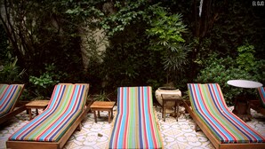 Un espace patio avec des chaises longues à rayures et une petite table, le tout entouré d’une végétation luxuriante.