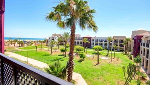 Une cour d’hôtel agrémentée de palmiers, avec une piscine et une vue sur la mer.