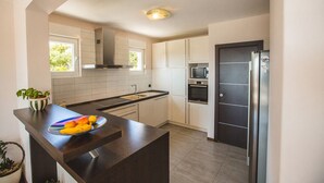 Una cocina moderna con armarios blancos, un refrigerador de acero inoxidable, un microondas y un horno empotrado. Hay una encimera de madera con un bol de fruta.
