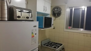 Una cocina compacta con refrigerador, microondas, estufa a gas y ventilador.