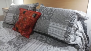 Una cama con ropa de cama de diseño gris y rojo, un cabecero de madera y una mesita de noche con una lámpara.