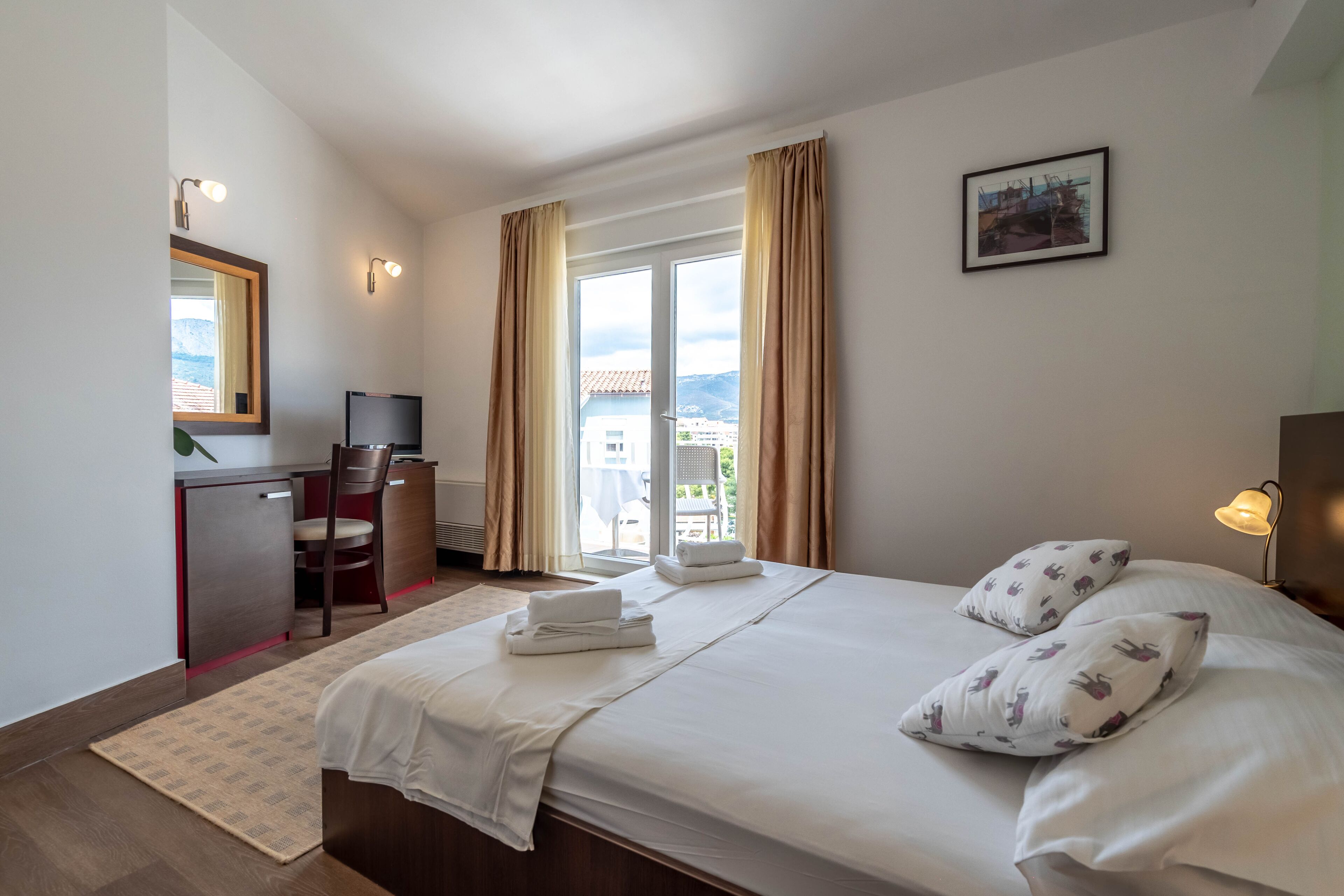 A hotel room with a bed, a desk, a chair, a TV, and a window with curtains.