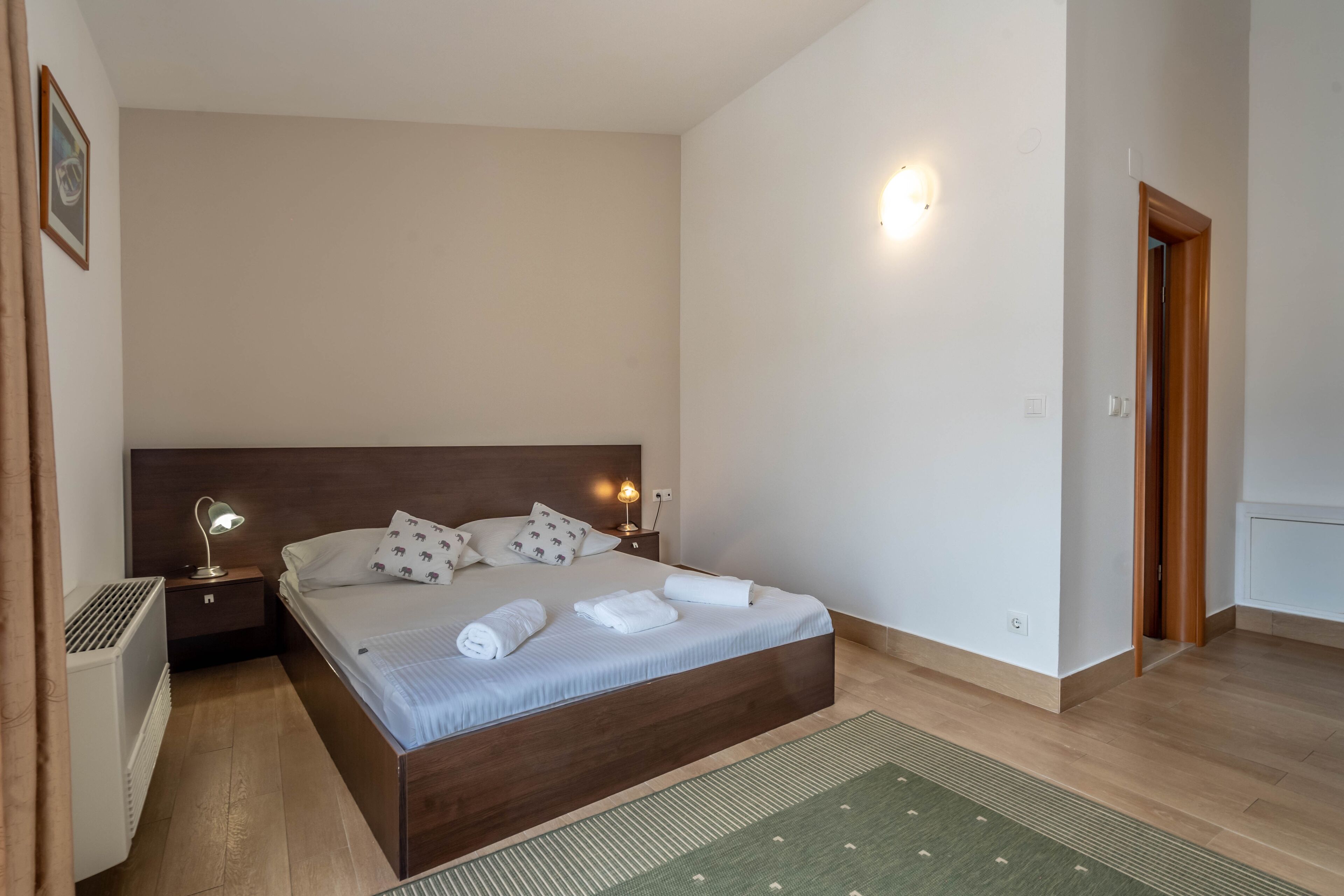 Ein Schlafzimmer mit einem großen Bett, Nachttischlampen, einem Heizkörper und einem grünen Teppich.
