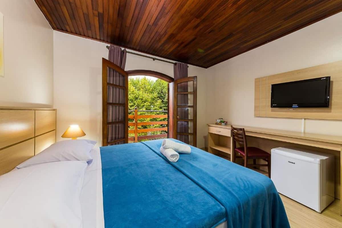 Un dormitorio con cama, escritorio, silla, televisor y un refrigerador pequeño.