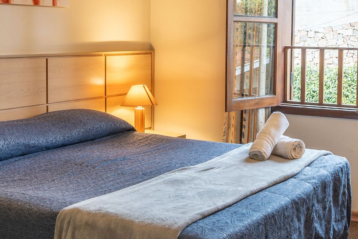 Un dormitorio con una cama grande, una mesita de noche, una lámpara, una ventana con cortinas y un cuadro en la pared.