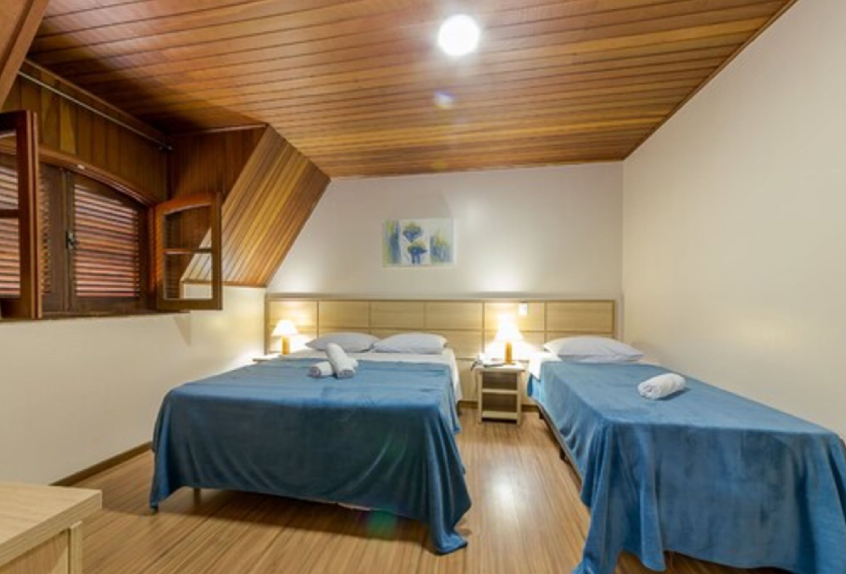 A room with two beds, wooden ceiling, and a painting on the wall.