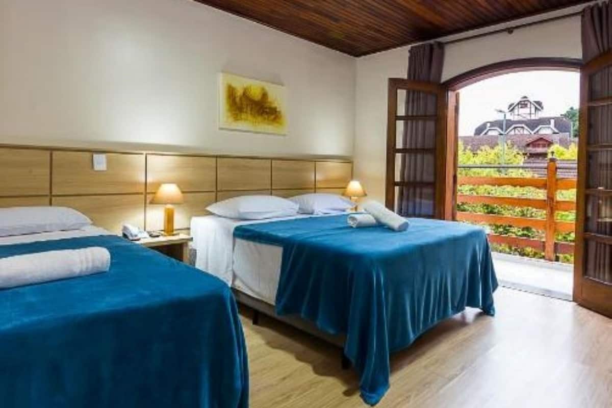 Habitación de hotel con dos camas, techo de madera y vista a un edificio a través de una puerta abierta.