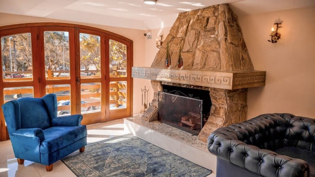 A living room with a stone fireplace, blue armchairs, and a view through large glass doors. - Hotel Euro Suite Campos do Jordão (Campos do Jordão)