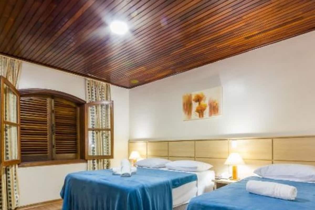 Habitación de hotel con dos camas, suelo y techo de madera, y una ventana con cortinas.