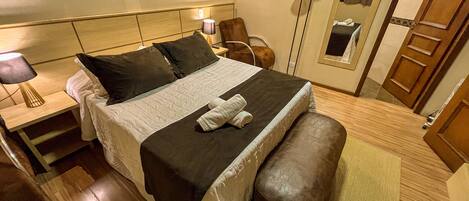Habitación de hotel con cama, mesita de noche, silla, lámpara de pie, espejo y armario.
