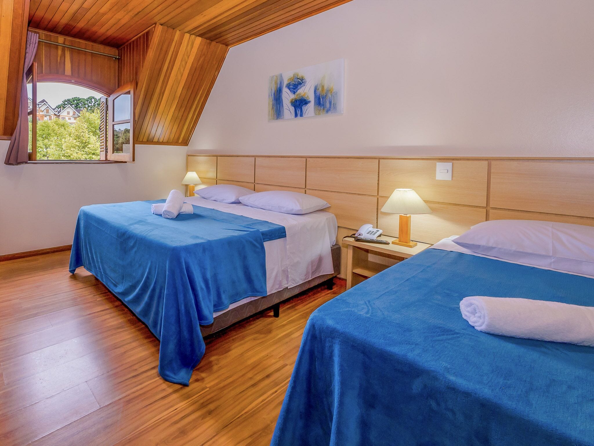 A hotel room with two beds, wooden flooring, a wooden ceiling, and a painting on the wall.