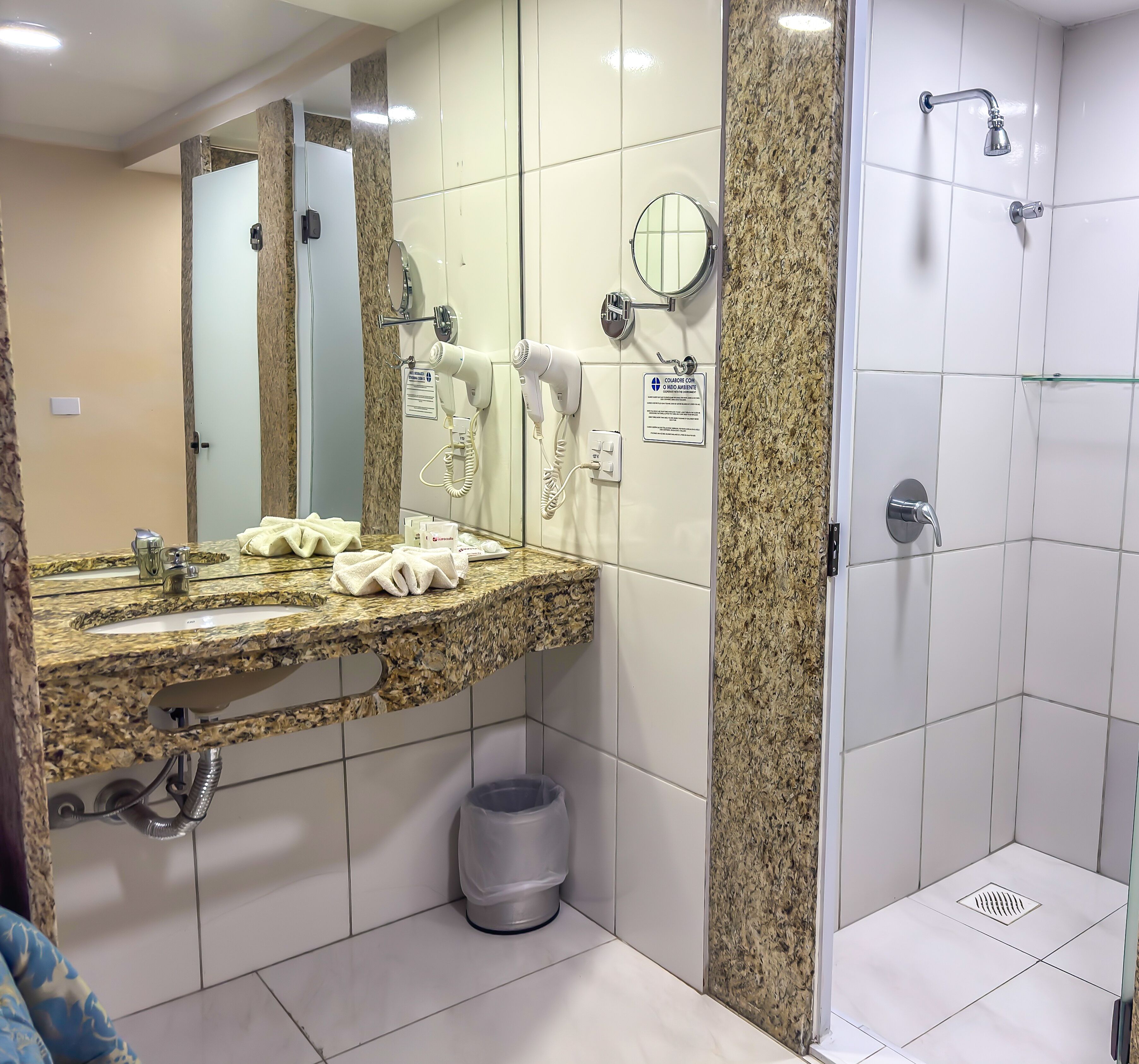 Een moderne badkamer met een granieten aanrecht, een spiegel, een handdoekrek, een haardroger en een douchehoek.