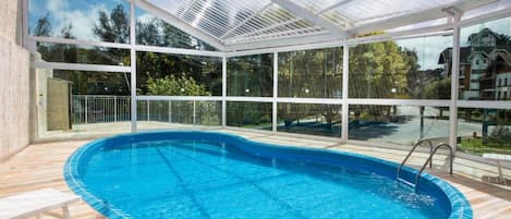 Une piscine dotée d’une enceinte en verre, entourée d’une terrasse en bois et d’une rambarde en métal.