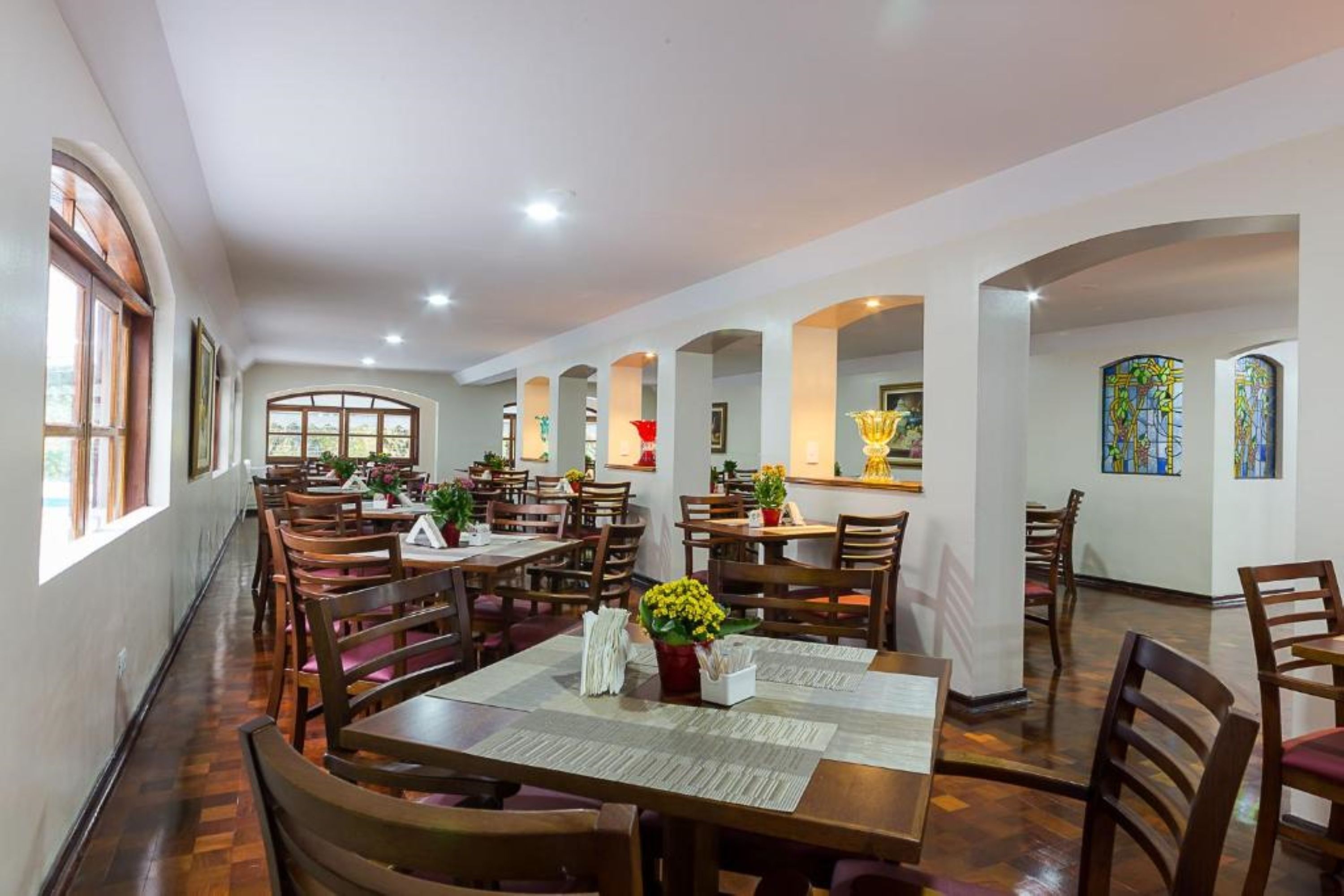 A spacious dining area with multiple tables and chairs, large windows, and decorative stained glass windows.