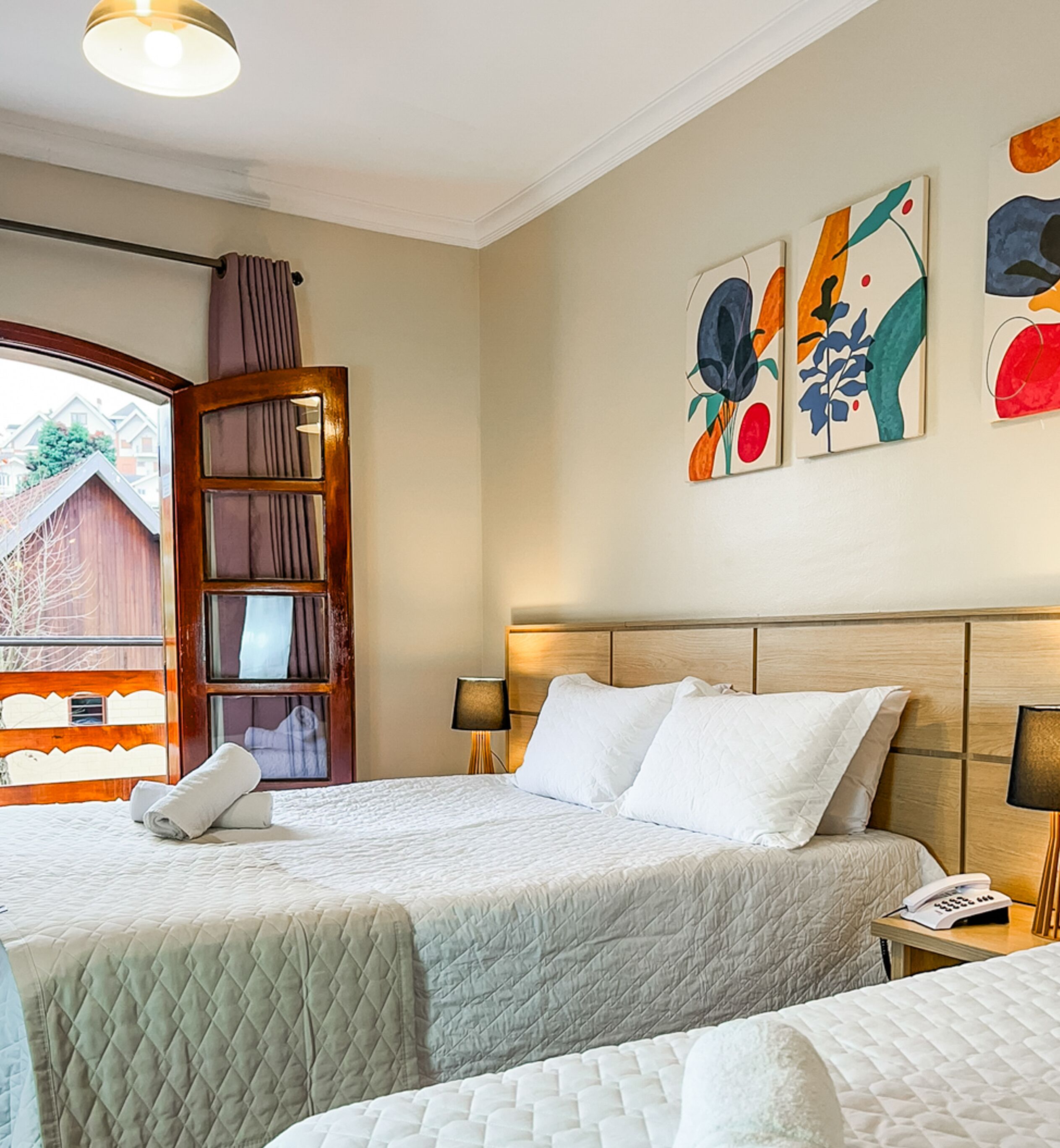 A hotel room with a large bed, a bedside table with a lamp, a wooden headboard, and abstract wall art.