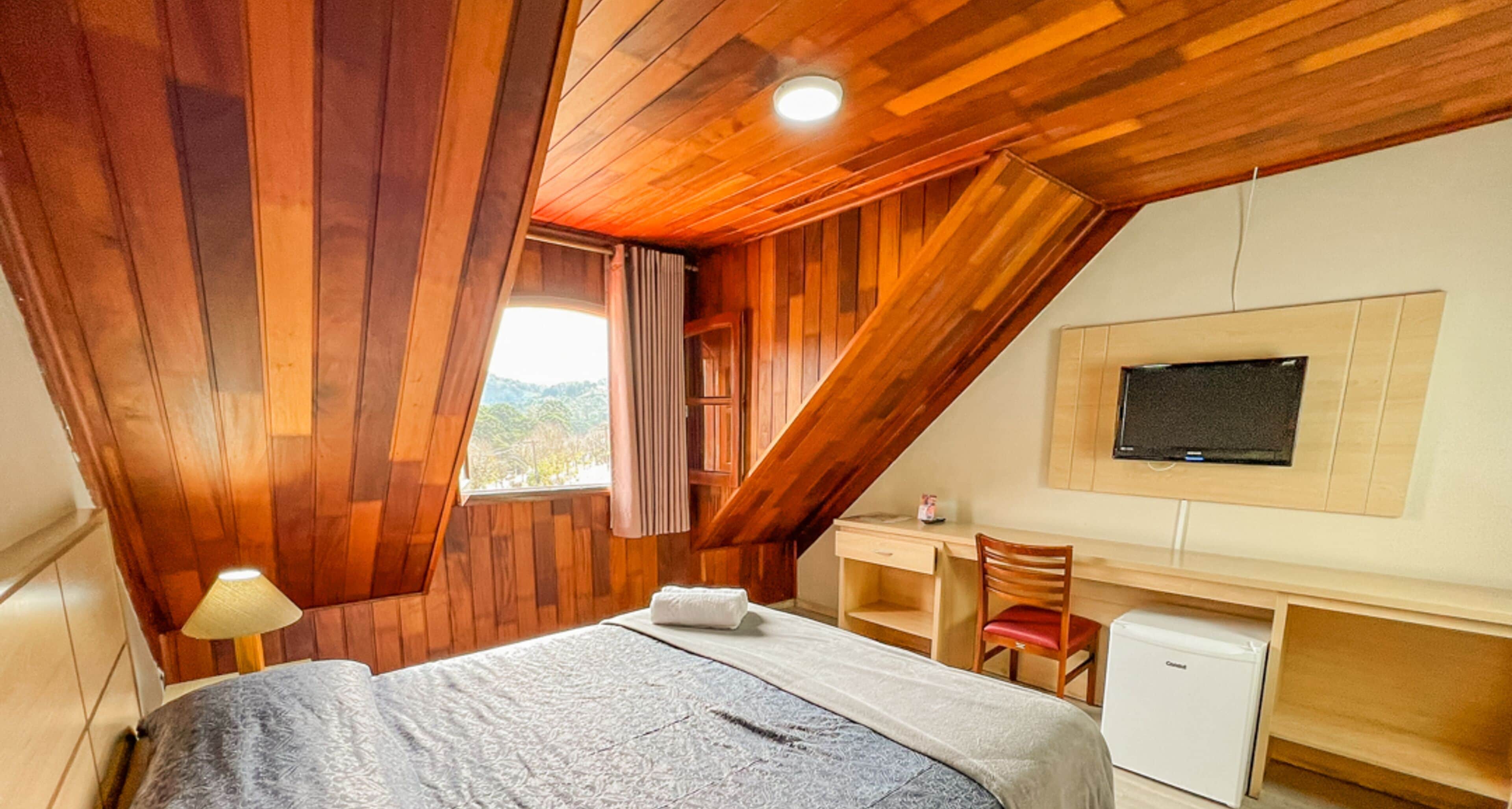 Un dormitorio con cama, escritorio, silla, televisor y un refrigerador pequeño.