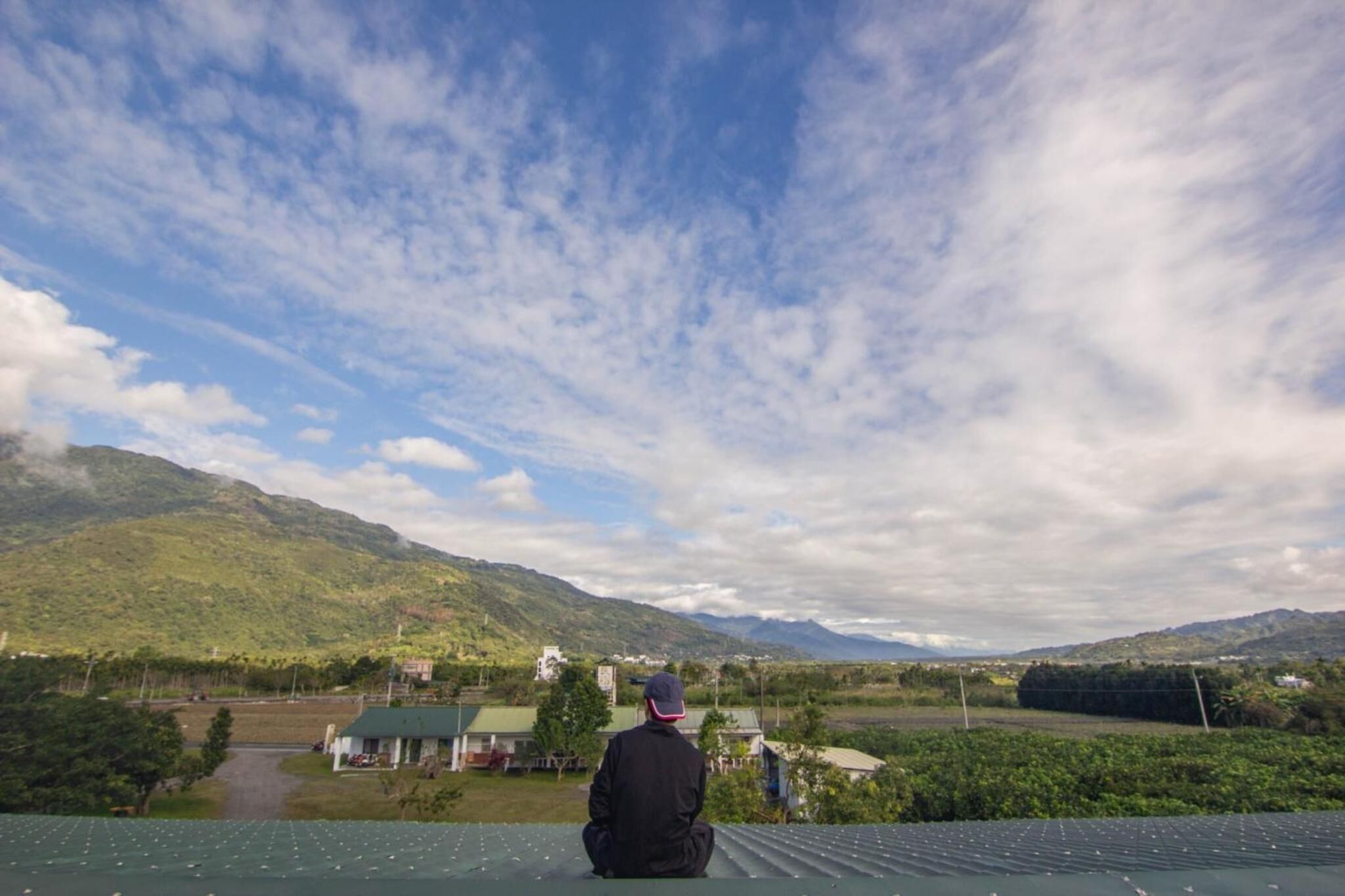 A person sitting on a roof overlooking a landscape with mountains and a river.