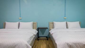 A room with two beds, each with white bedding and wooden headboards, against a blue wall.