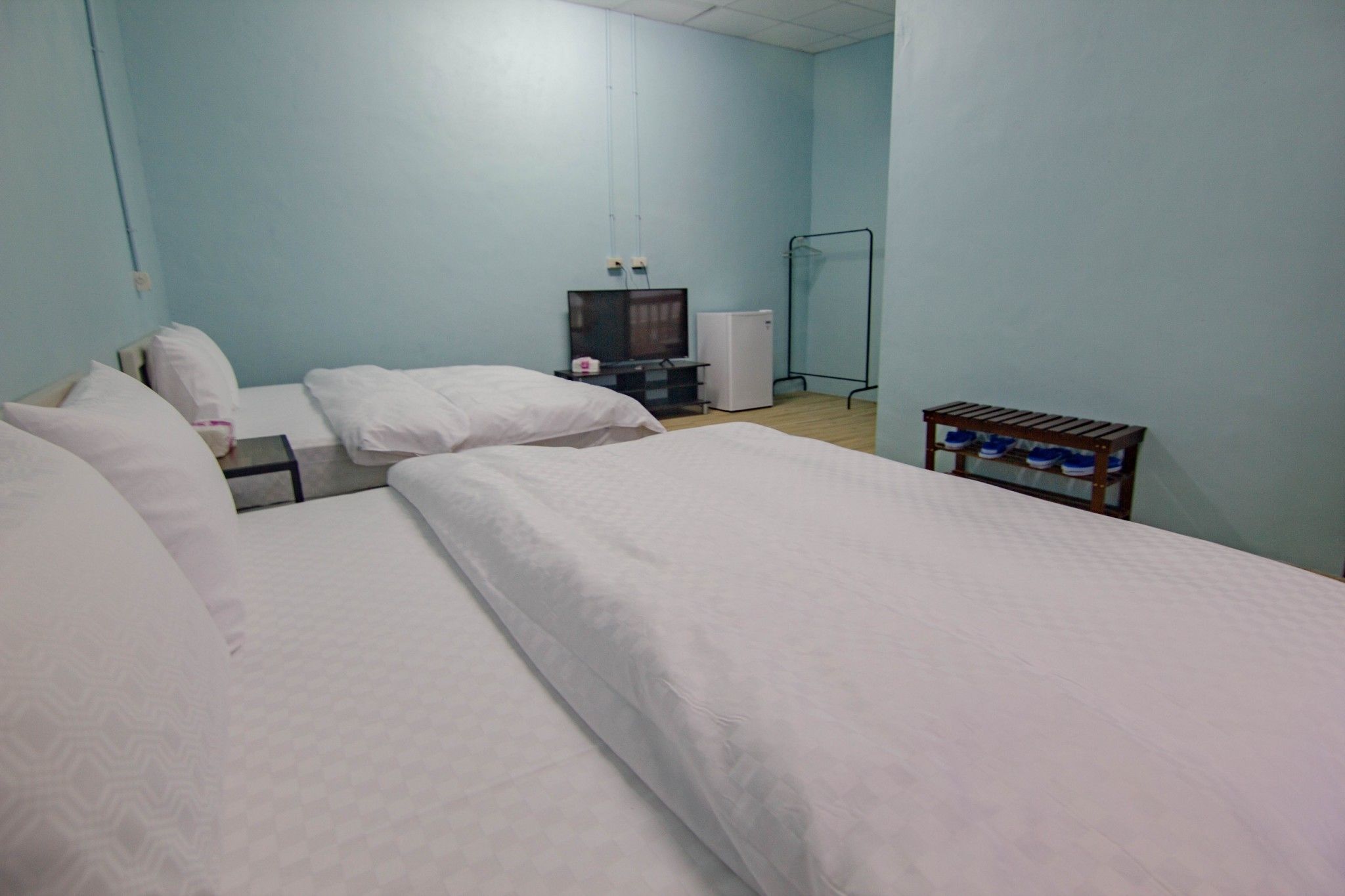Une chambre d’hôtel avec deux lits, une télévision, un petit réfrigérateur et un porte-chaussures.