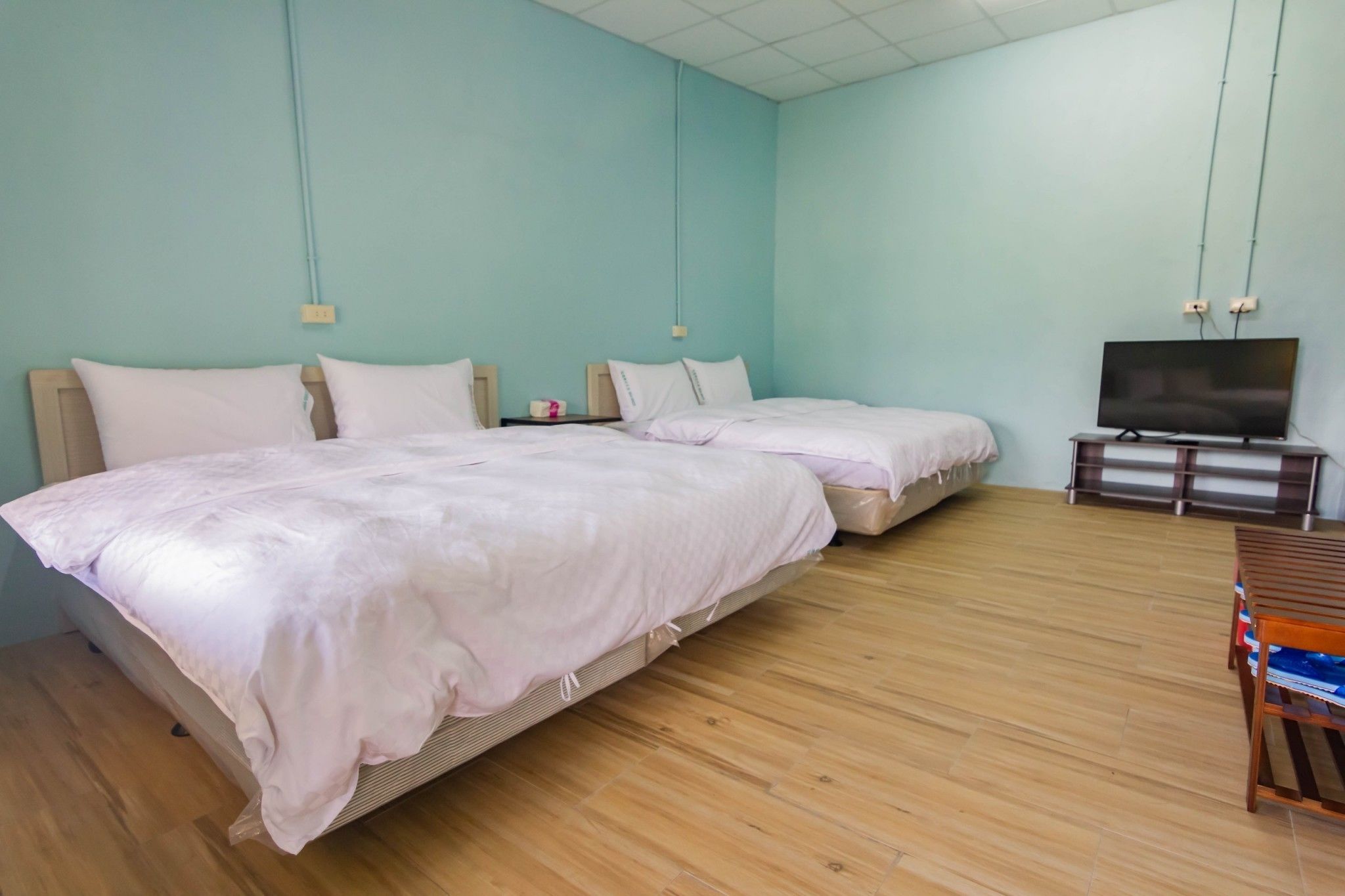 Hotellihuone, jossa on kaksi sänkyä, jalustalla oleva televisio ja puulattia.