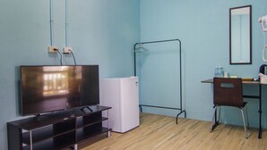 Ein Zimmer mit Fernseher, einem weißen Minikühlschrank, einem Schreibtisch mit Stuhl und einem Spiegel.