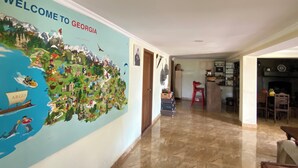 A hallway with a large welcome mural to Georgia, a kitchen area, and a dining area with a red chair. - Green House (Kutaisi)