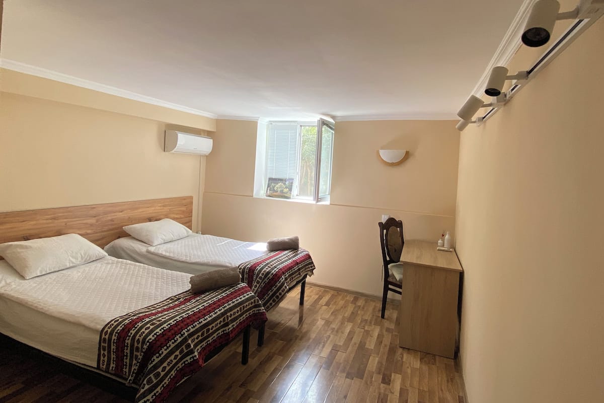 Habitación de hotel con dos camas, un escritorio, una silla, un ventanal y un equipo de aire acondicionado.