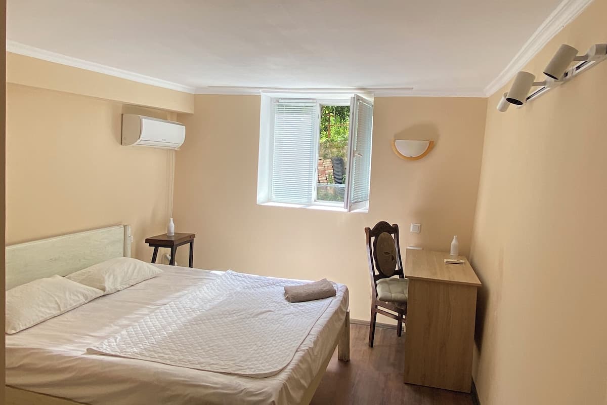 Un dormitorio con cama, escritorio, silla, ventana y equipo de aire acondicionado.
