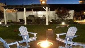 An outdoor patio area with a fire pit, Adirondack chairs, and a grill. - The Hamlet (Saratoga Springs)