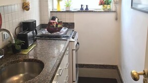 A compact kitchen with a granite countertop, a stainless steel sink, a stove, and a window with a view of the outside. - Studio Premium Leblon (Rio de Janeiro)