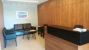 A reception area with a wooden reception desk, black sofas, and a small round table with chairs. - Studio Premium Leblon (Rio de Janeiro)