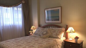 A bedroom with a floral bedspread, a nightstand with a lamp, and a framed picture on the wall. - Studio Premium Leblon (Rio de Janeiro)