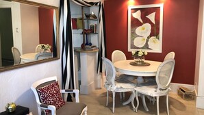A dining area with a round table and white chairs, a mirror, and a bookshelf with books and decorative items. - Studio Premium Leblon (Rio de Janeiro)