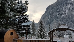 Eine Holzhütte mit schneebedecktem Dach, umgeben von schneebedeckten Bäumen und einer Bergkulisse.