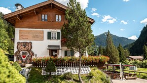 Eine Holzhütte mit einer Bärenmalerei, umgeben von viel Grün und Bergen.