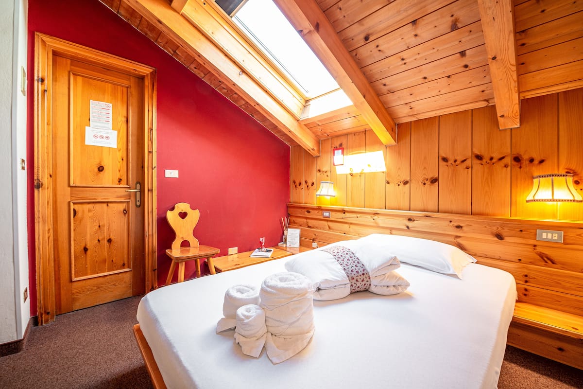 A wooden-paneled room with a bed, towels, a wooden door, and a red wall.