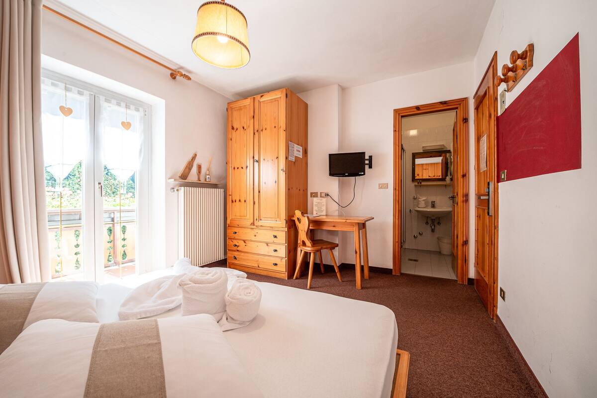 A hotel room with a bed, a desk, a wardrobe, a television, and a bathroom visible through an open door.