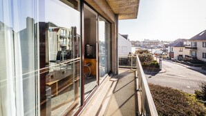 Un edificio moderno con amplios ventanales, un balcón con mobiliario exterior y vistas a una calle residencial.
