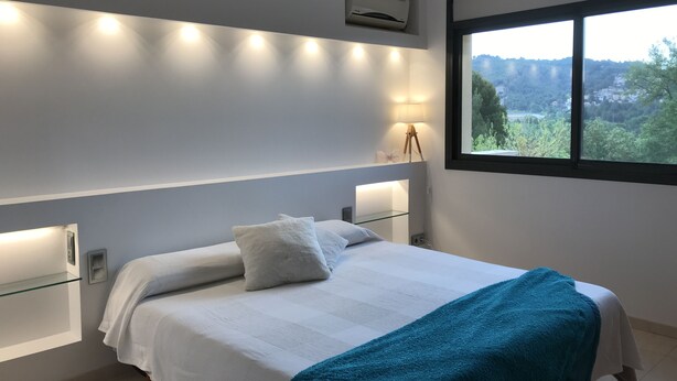 Un dormitorio moderno con cama, lámparas de noche, aire acondicionado y ventana con vista a follaje.