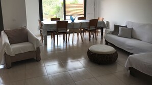 Una sala de estar con comedor, un sofá, una silla y un otoman redondo.