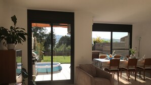 Amplia sala de estar con puerta de vidrio corrediza que da a un balcón, un sofá cómodo, una mesa de comedor con sillas y una piscina pequeña.