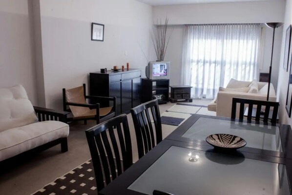 A living room with a sofa, chairs, a dining table, a TV, and a lamp.