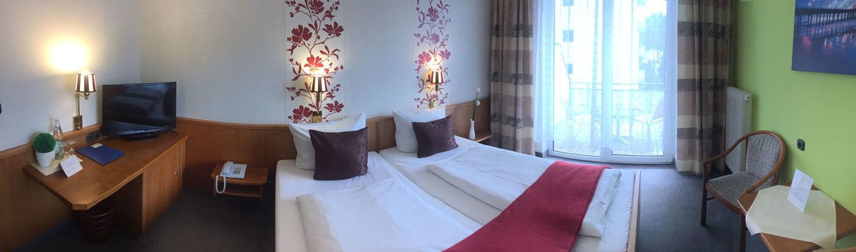 A hotel room with a bed, a desk with a TV, a lamp, and a chair.