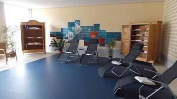 Une pièce avec un sol bleu, plusieurs fauteuils inclinables, un buffet en bois et un mur recouvert de carreaux décorés d’œuvres d’art.