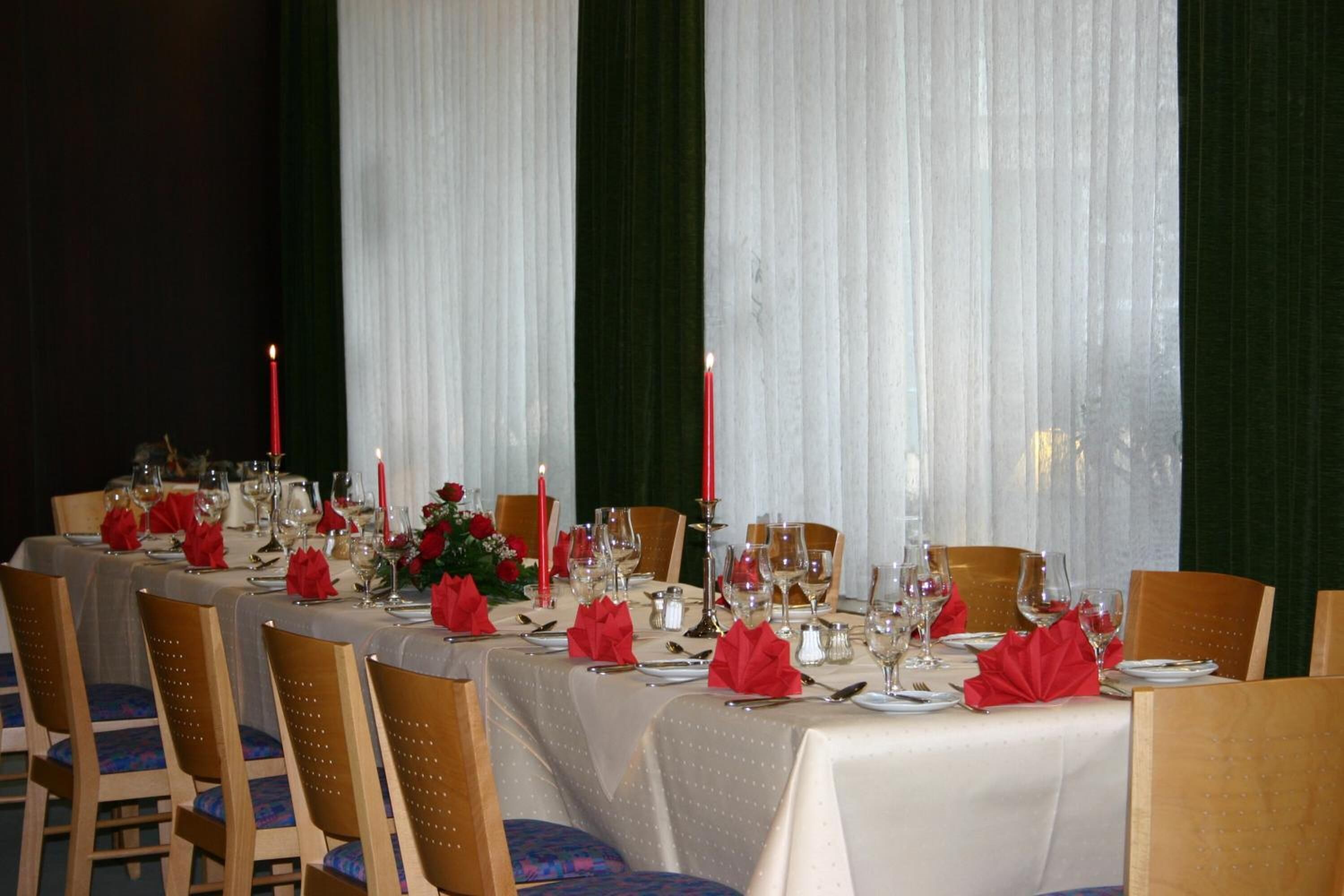 A long dining table set for a formal meal with multiple chairs, candles, and red napkins.