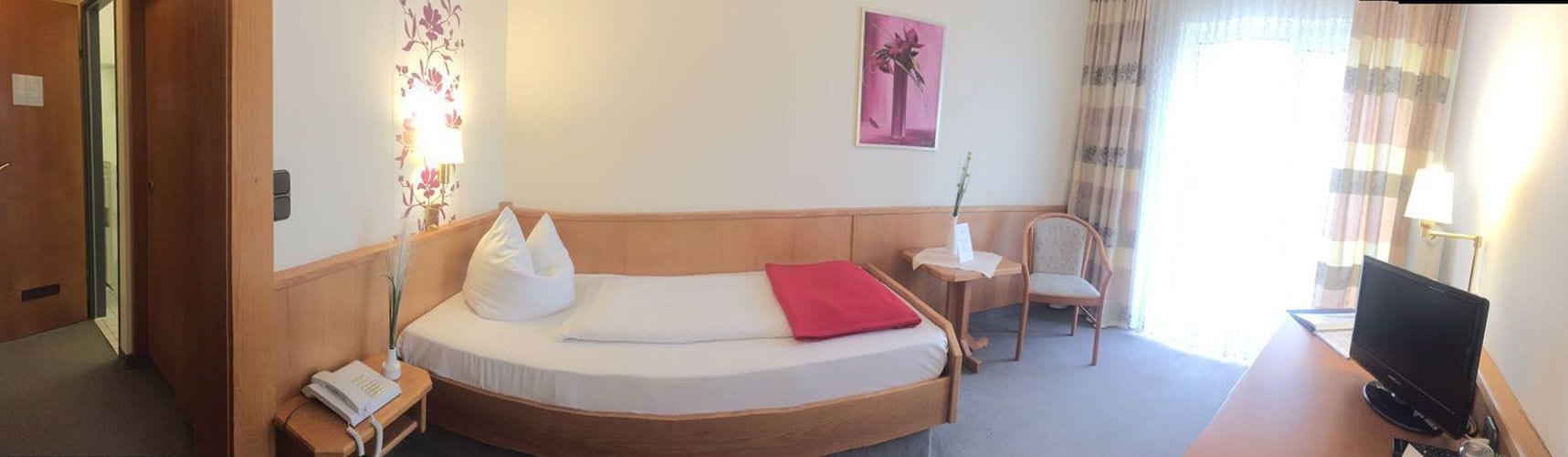 Een hotelkamer met een gebogen bed, een bureau met een computer, een stoel en een televisie.