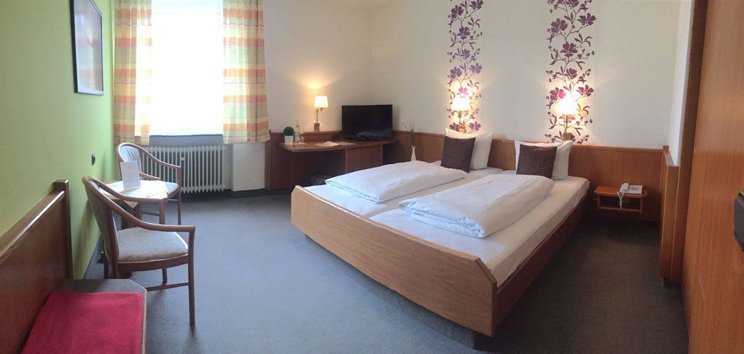 A hotel room with a large bed, a desk with a chair, a television, and a small table with a lamp.