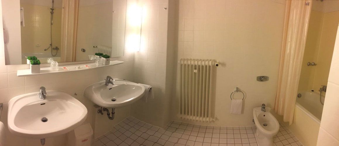 Een badkamer met twee wastafels, toilet, bidet, spiegel en een handdoekradiator.