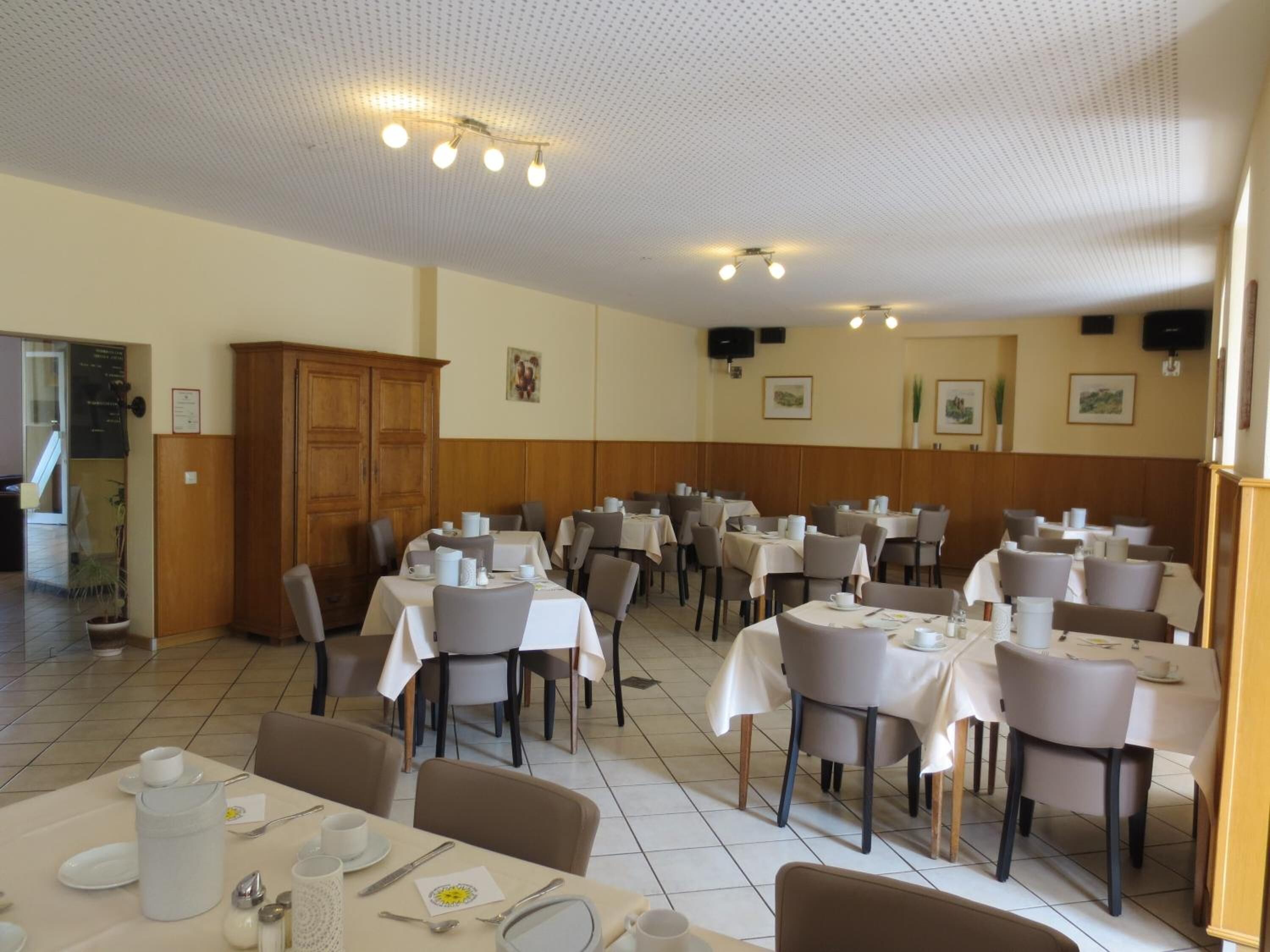 A dining area with multiple tables and chairs, a wooden cabinet, and ceiling lights.