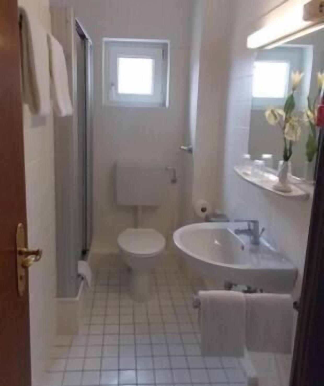Ein kleines, kompaktes Badezimmer mit Toilette, Waschbecken und einem Fenster über der Toilette.